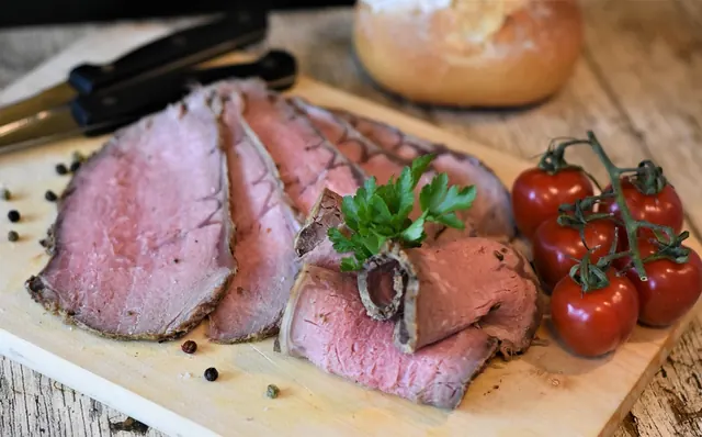 Rosbife fatiado na tábua de madeira, com tomate ao lado